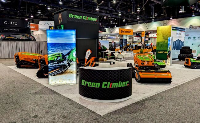 Green Climber completed booth: a circular hanging sign above an open floor displaying compact tracked machines
