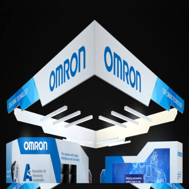 Omron booth with a white angular hanging sign and a suspended geometric lighting structure.