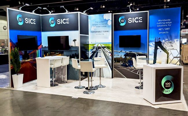 SICE completed booth: three tall display panels with screens, counters and café tables