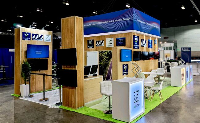 Kozut completed booth: an overhead frame supported by tall display columns around an open meeting area