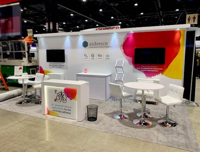 Aidence completed booth: an angular overhead frame above product graphics and reception counters