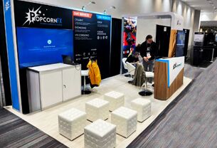 Popcorn FX completed booth: a corner graphic wall with a reception counter, low tables and cube stools
