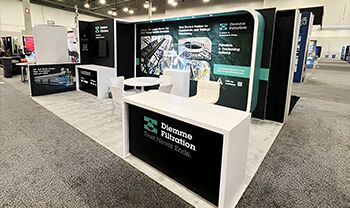 Diemme Filteration completed booth: a curved graphic panel behind a reception counter and meeting table