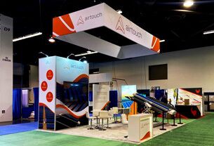 Airtouch Solar completed booth: a suspended angular sign above tilted solar panels and demonstration tables
