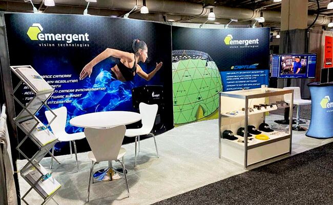 Emergent Vision Technologies completed booth: a curved graphic back wall behind product displays, tables and stools