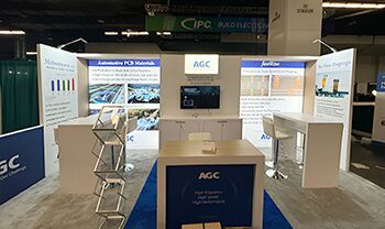 AGC Multi Material America completed booth: a broad back wall with display panels, a central counter and café tables