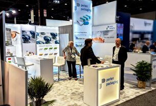 Perlen Packaging completed booth: a hanging sign above product-display panels, a counter and meeting chairs