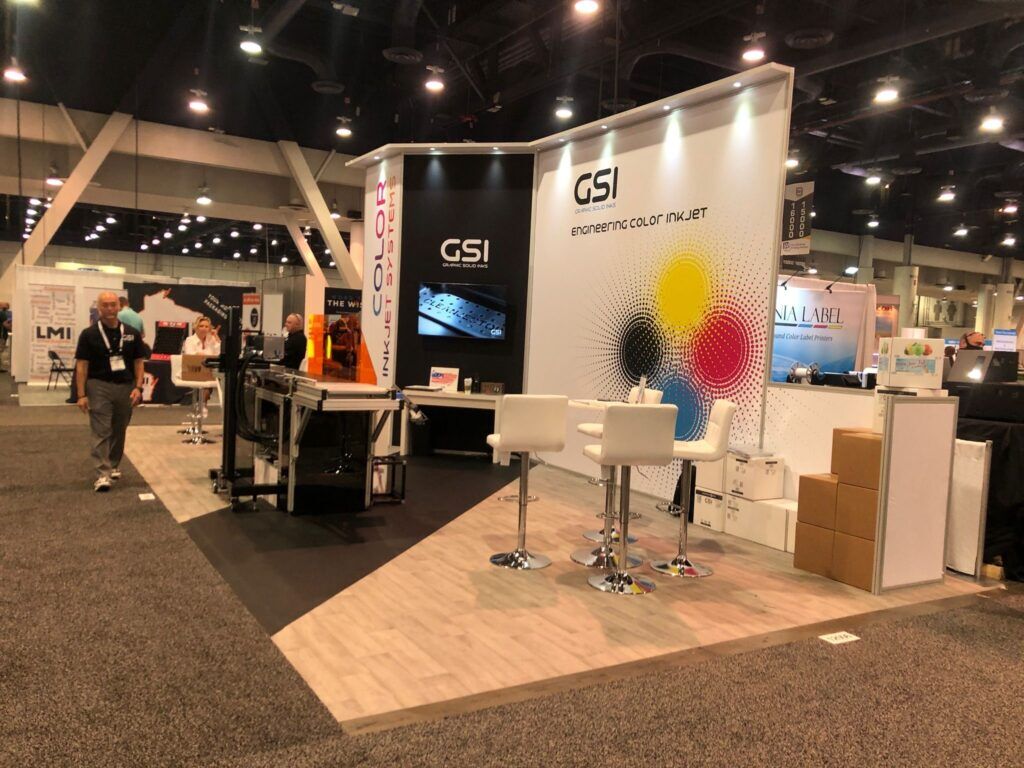GSI completed booth: a curved wall with circular graphics behind a reception counter and stools