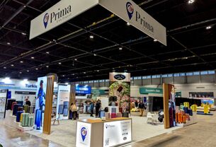 Prima USA completed booth: a rectangular hanging sign above freestanding product displays and counters