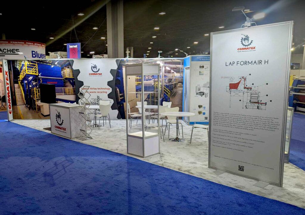 Cormatex completed booth: a wide graphic back wall behind a reception counter and meeting area