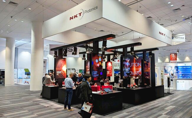 NKT Photonics completed booth: a broad canopy over graphic walls, product displays and a seating area