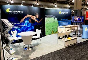 Emergent Vision Technologies completed booth: a curved graphic back wall behind product displays, tables and stools