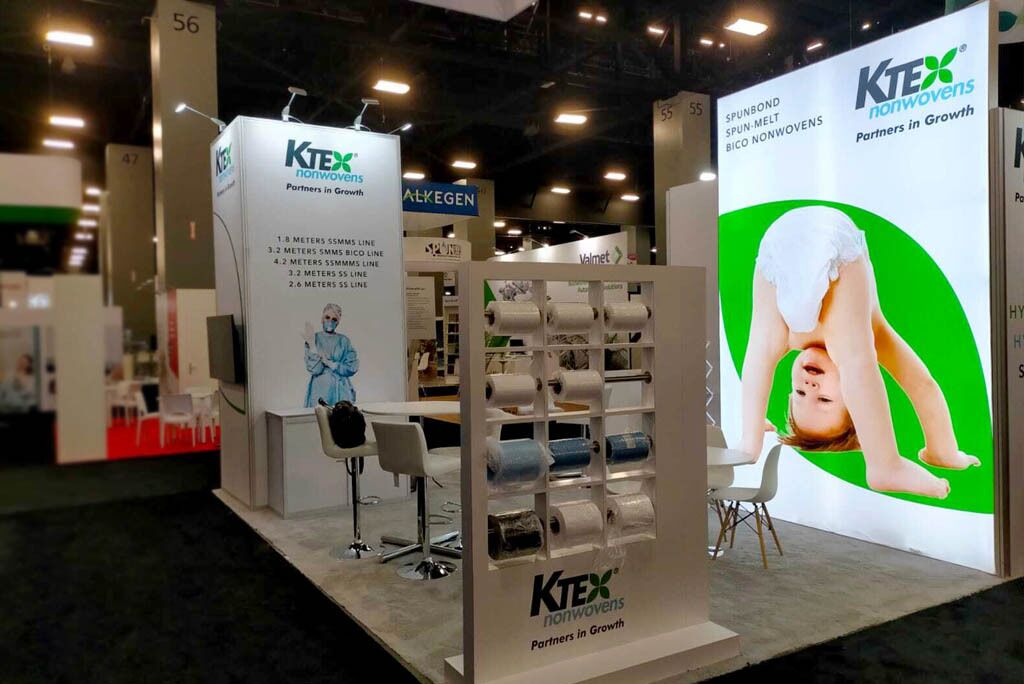 KTEX Nonwovens completed booth: a rectangular hanging sign above tall botanical graphics and a reception desk