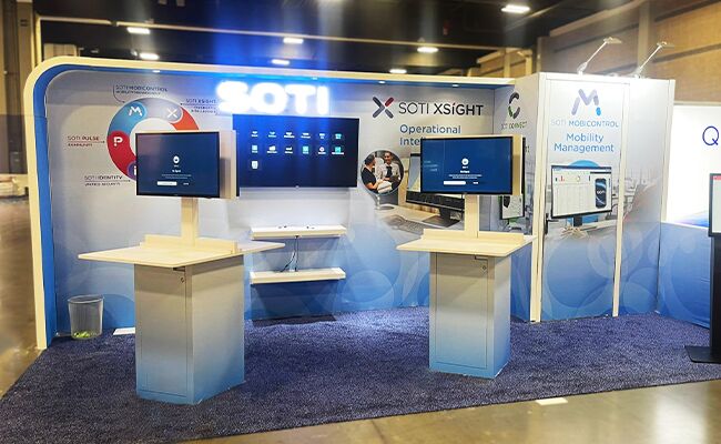 SOTI completed booth: a screen in the back wall above a reception counter and seating area