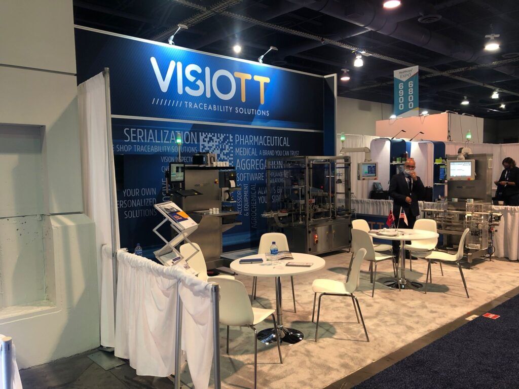 VISIOTT completed booth: a large graphic wall beside transparent framed panels and a meeting table