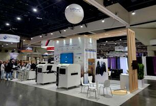 IPC APEX exhibit completed booth: a wood-slat arch framing glass product displays and a meeting table