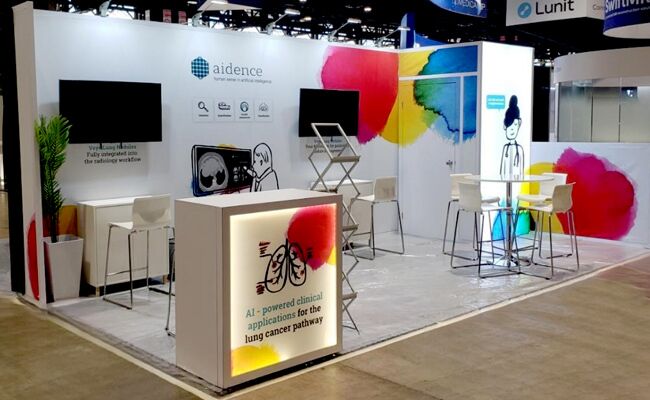 AIDENCE completed booth: an angular overhead frame surrounding product shelves and a reception counter