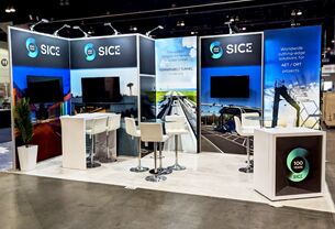 SICE completed booth: three tall display panels with screens, counters and café tables