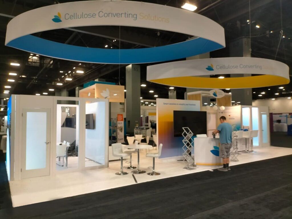 Cellulose Converting Solutions completed booth: overlapping curved hanging signs above display walls and glass counters