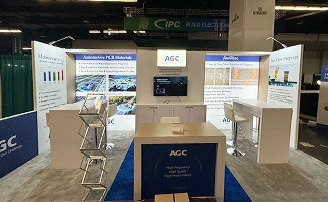 AGC Multi Material America completed booth: a broad back wall with display panels, a central counter and café tables