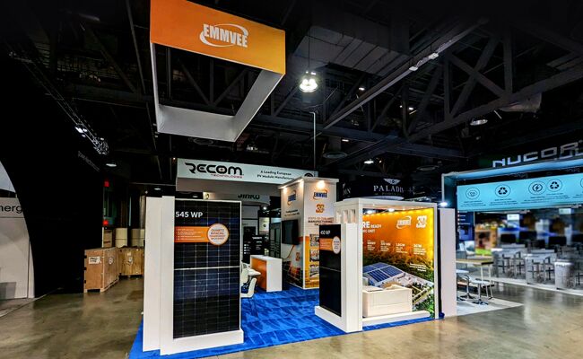 Emmvee completed booth: a rectangular hanging sign above upright solar panels and counters