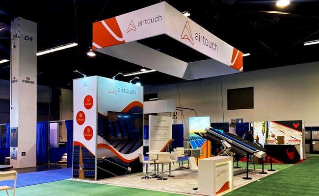 Airtouch Solar completed booth: a suspended angular sign above tilted solar panels and demonstration tables