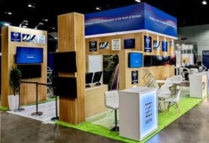 Kozut completed booth: an overhead frame supported by tall display columns around an open meeting area