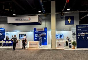Shemesh Automation completed booth: a rectangular hanging sign above a central display wall and equipment stations