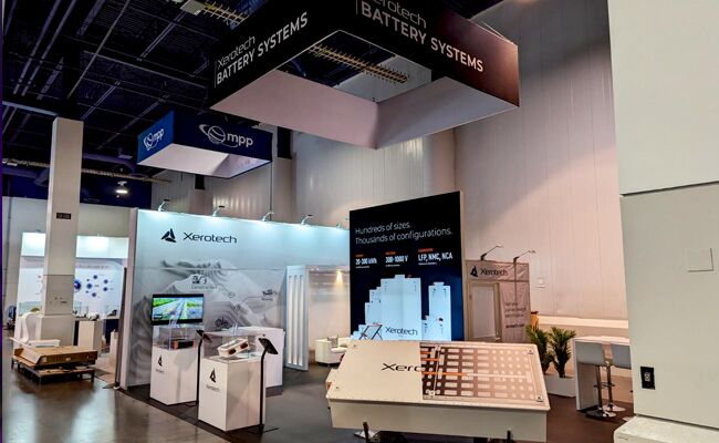 Xerotech completed booth: a suspended rectangular sign above demonstration counters and a video wall