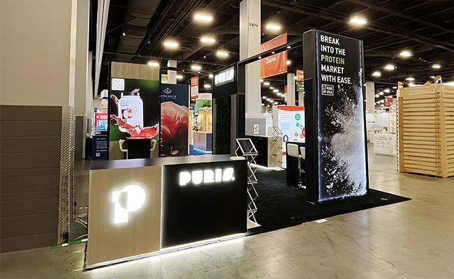 Puris completed booth: a rectangular overhead frame above product shelving and a reception desk
