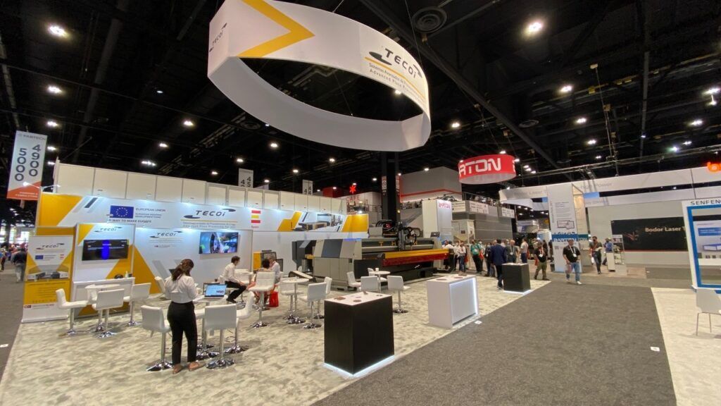 TECOI completed booth: a large circular hanging sign above industrial demonstration equipment