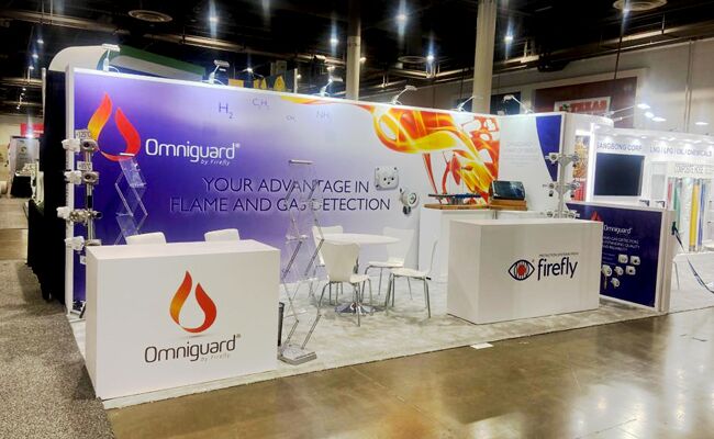 Firefly completed booth: a sweeping graphic back wall behind an angular counter and meeting tables